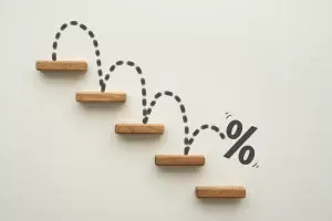 Wooden ledges on a wall with a drawn percent symbol bouncing down them like steps, illustrating an interest rate declining, which Jade Finance can leverage for personal and commercial loans.